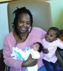 Maryland EXCELS provider Pamela Funderburk sits holding an infant and her arm around a little boy.