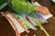 A child glues colorful strips of paper while making a craft.