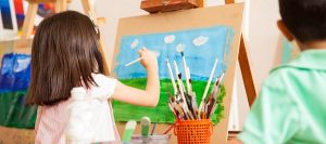 preschooler, painting with water color on canvas standing on easel