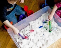 Two children paint ice cubes in a large plastic tub