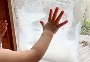 A child plays with a bag full of bubbles that is taped to a window.