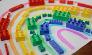 Legos are arranged by color on an outline of a rainbow drawn on paper