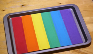 Strips of colored paper are arranged in a rainbow pattern on a tray