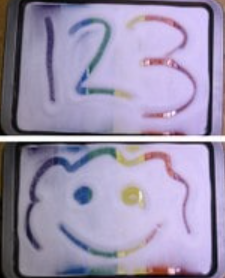 The numbers one, two and three, and a smiley face are drawn in trays of salt to reveal colors underneath.