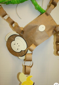 A toy monkey made from a paper lunch bag with arms made from strips of brown paper linked together