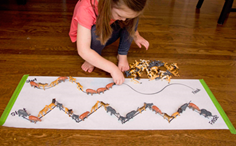 A young child lining up toy animals on lines drawn on a large sheet of white paper