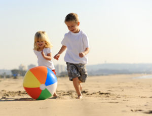 Two young children playing with a beach ball at the beach