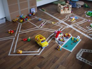 Toy cars and trucks are on a racetrack made from tape on a floor