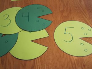 Pieces of green paper cut into shapes like lily pads with numbers written on each piece.