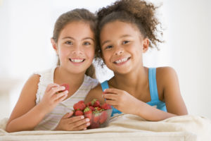 Two girls smiling and sharing a bowl of strawberries