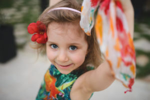 A young girl wearing a headband with a red flower waves a colorful scarf